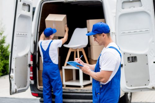 Two removal company workers unloading boxes from minibus into new home.