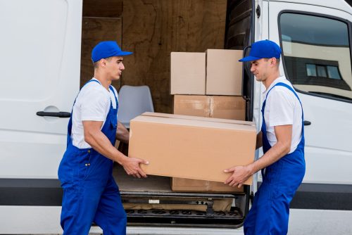 Two removal company workers unloading boxes from minibus into new home.